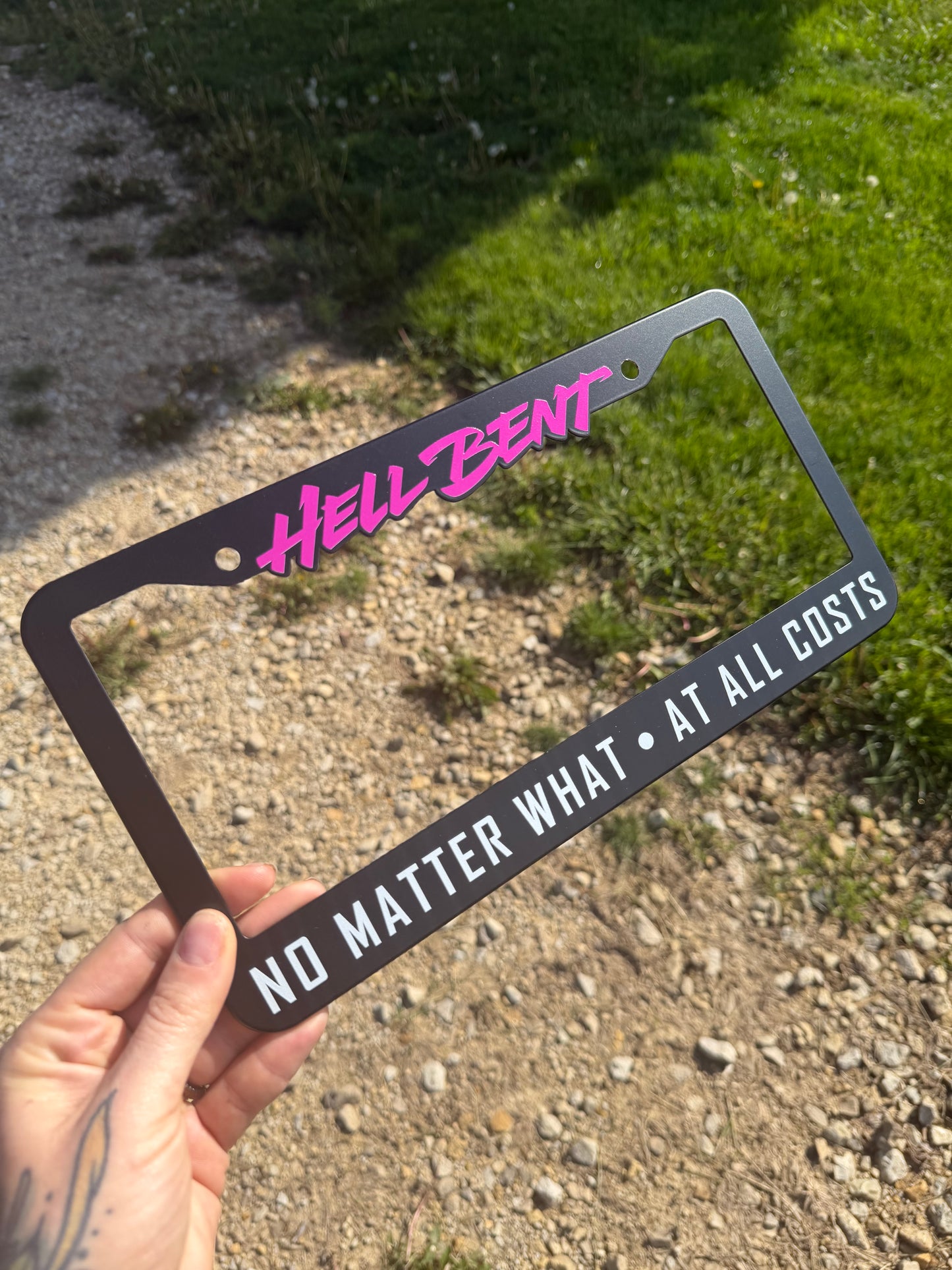 Hell Bent NO MATTER WHAT - AT ALL COSTS license plate frame. All-metal (NOT plastic) high quality allow frame with a smooth matte black finish, featuring bright magenta and white text accents!

Sized 12.2in W x 6.3in H (31cm W x 16cm H) with a 0.55in (1.4cm) border along the top, and 1in (2.5cm) border along the bottom.&nbsp; Screw holes are 6.69in (17cm) apart.

This fully metal plate frame will outlast any cheap plastic frames, and stand the test of time to keep you and your license plate looking fly as h