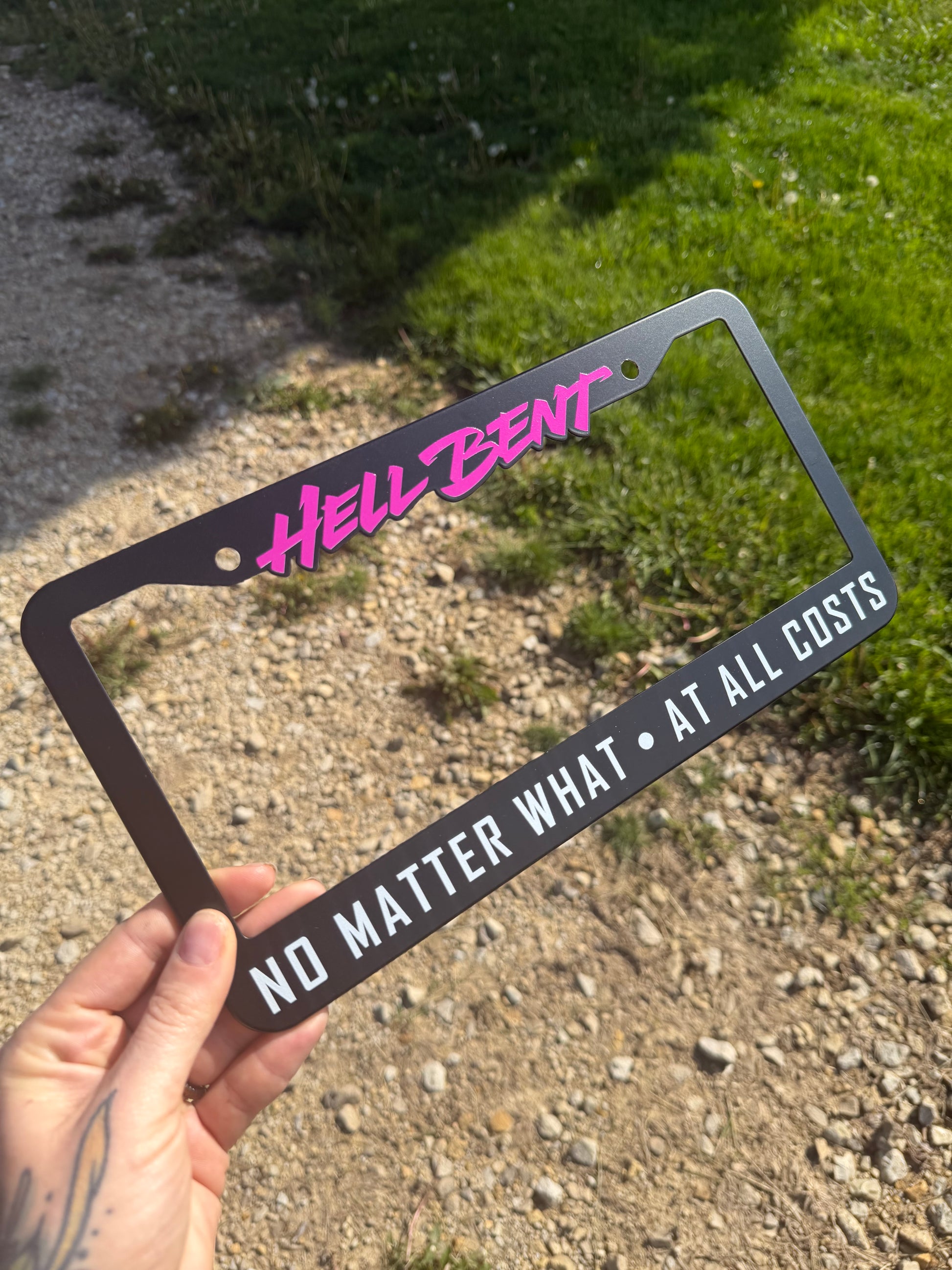 Hell Bent NO MATTER WHAT - AT ALL COSTS license plate frame. All-metal (NOT plastic) high quality allow frame with a smooth matte black finish, featuring bright magenta and white text accents!

Sized 12.2in W x 6.3in H (31cm W x 16cm H) with a 0.55in (1.4cm) border along the top, and 1in (2.5cm) border along the bottom.&nbsp; Screw holes are 6.69in (17cm) apart.

This fully metal plate frame will outlast any cheap plastic frames, and stand the test of time to keep you and your license plate looking fly as h