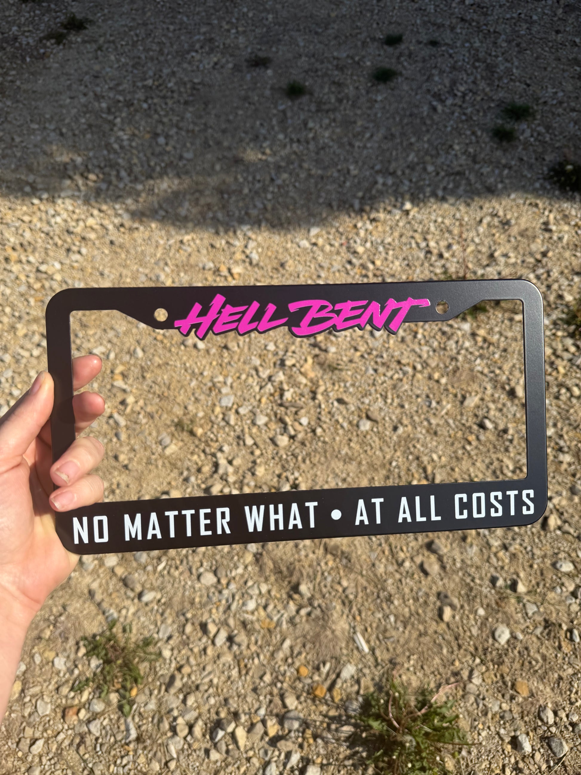 Hell Bent NO MATTER WHAT - AT ALL COSTS license plate frame. All-metal (NOT plastic) high quality allow frame with a smooth matte black finish, featuring bright magenta and white text accents!

Sized 12.2in W x 6.3in H (31cm W x 16cm H) with a 0.55in (1.4cm) border along the top, and 1in (2.5cm) border along the bottom.&nbsp; Screw holes are 6.69in (17cm) apart.

This fully metal plate frame will outlast any cheap plastic frames, and stand the test of time to keep you and your license plate looking fly as h